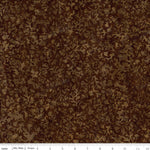 A close-up of a brown and tan abstract camouflage or leaf-like patterned fabric, with a white measuring ruler along the bottom edge showing scale.