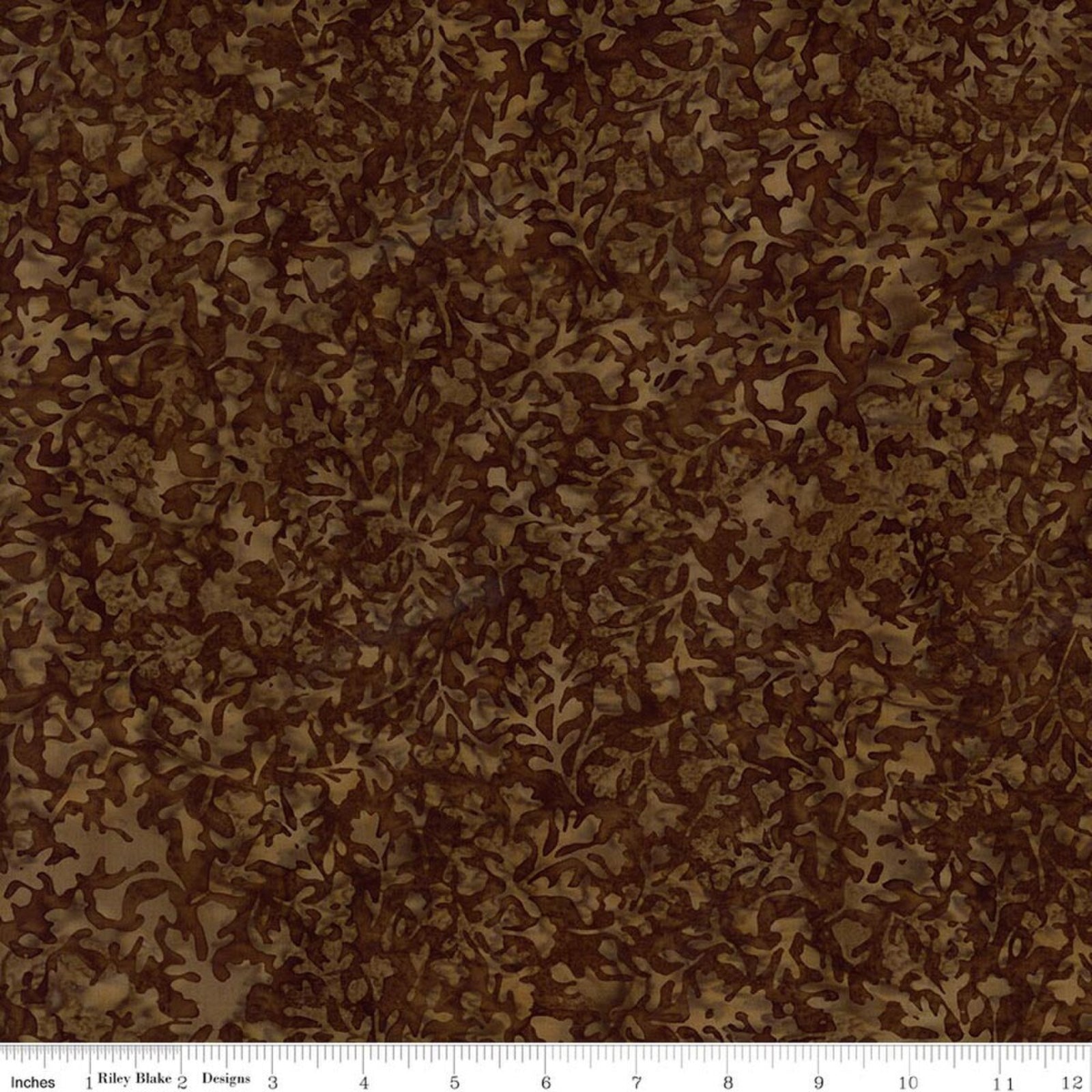 A close-up of a brown and tan abstract camouflage or leaf-like patterned fabric, with a white measuring ruler along the bottom edge showing scale.