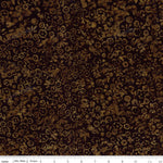A close-up of a dark brown and black batik fabric with a repeating floral and vine pattern, featuring a white ruler at the bottom indicating scale.