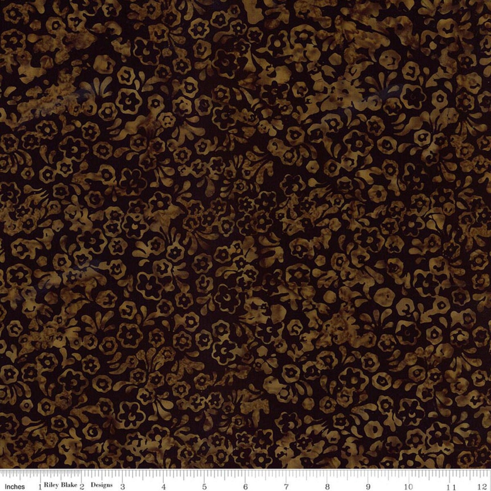 A close-up of a dark brown and black batik fabric with a repeating floral and vine pattern, featuring a white ruler at the bottom indicating scale.