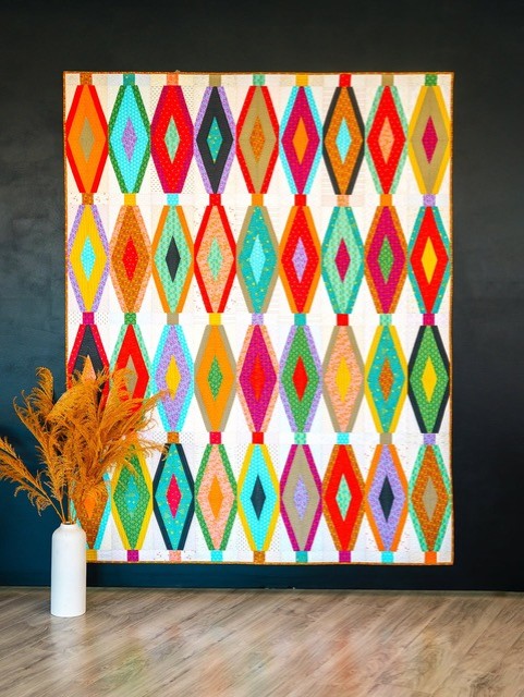 Breezeway quilt with bright layered diamond blocks displayed against a dark wall.