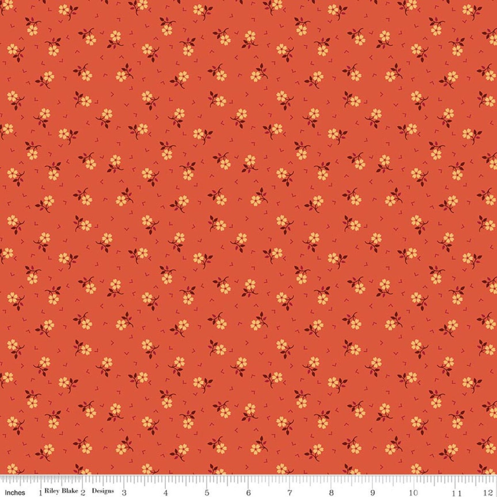 A repeating fabric pattern on a warm rust-orange background with small yellow flowers, dark brown stems, and tiny pink accents, shown with a ruler along the bottom edge.