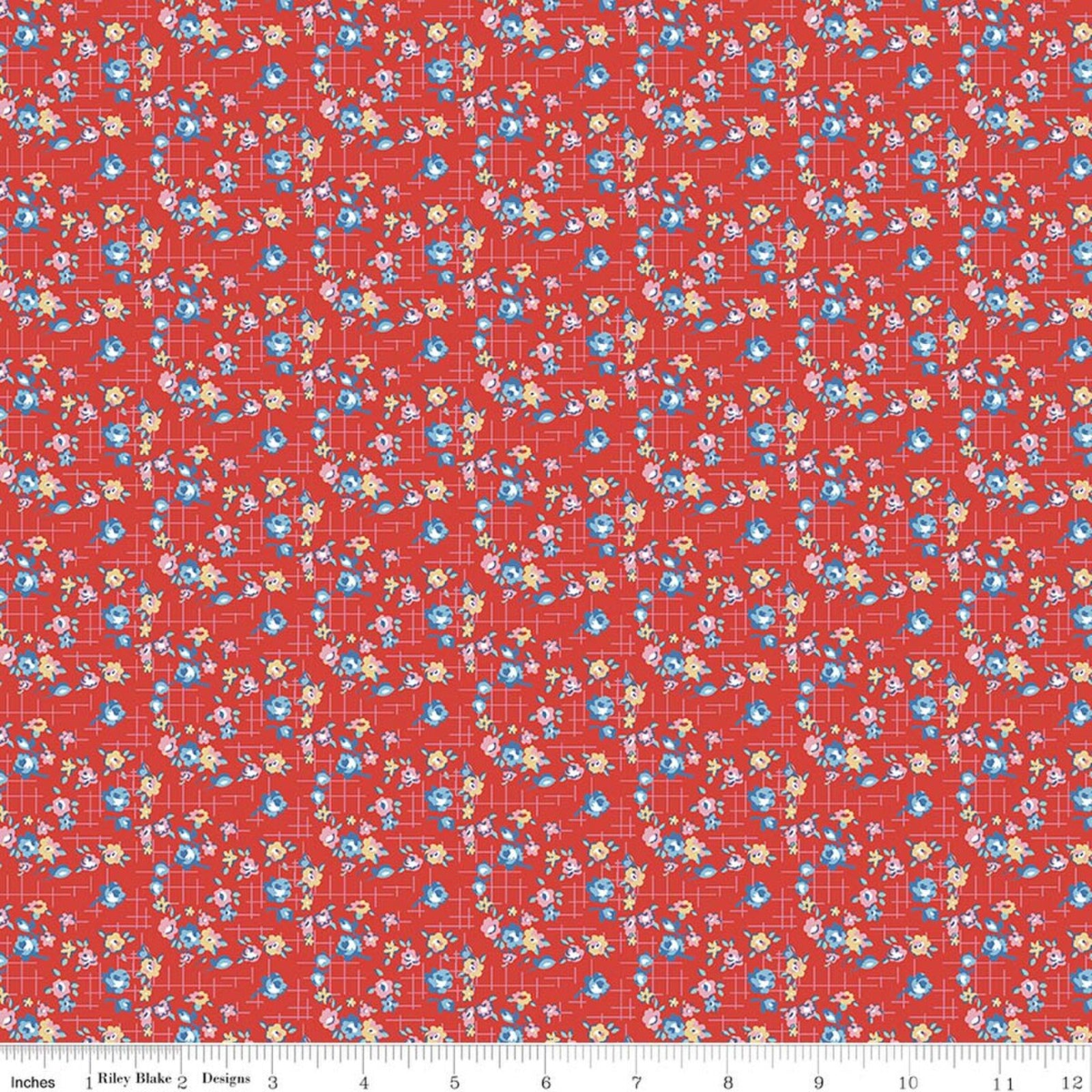 Red fabric with a dense repeating floral and geometric pattern in blue, yellow, and white, shown flat with a ruler along the bottom edge.