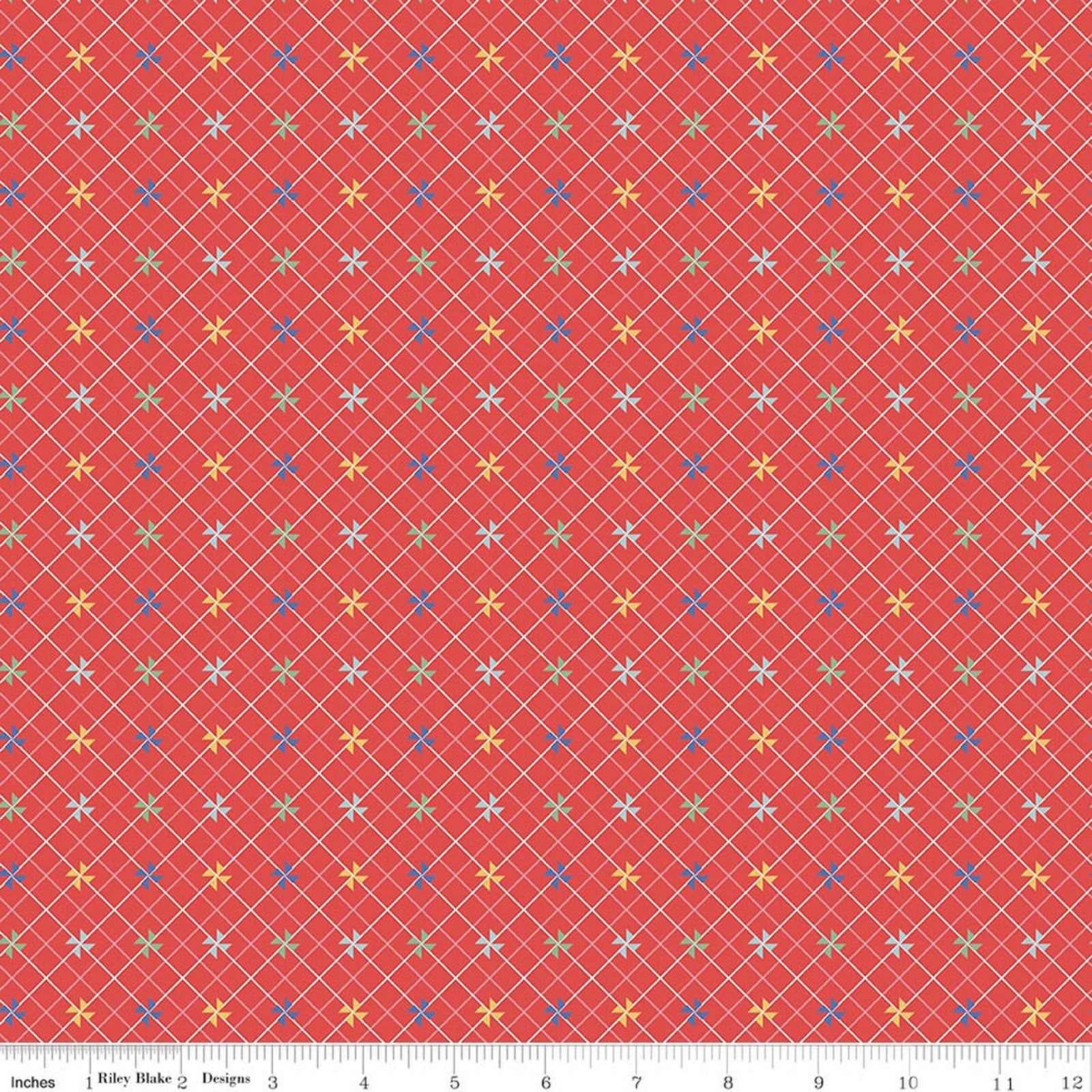 A close-up of a fabric pattern featuring a coral red background with a white diagonal grid and small multicolored star motifs in yellow, blue, green, and white. A ruler scale is visible along the bottom edge.