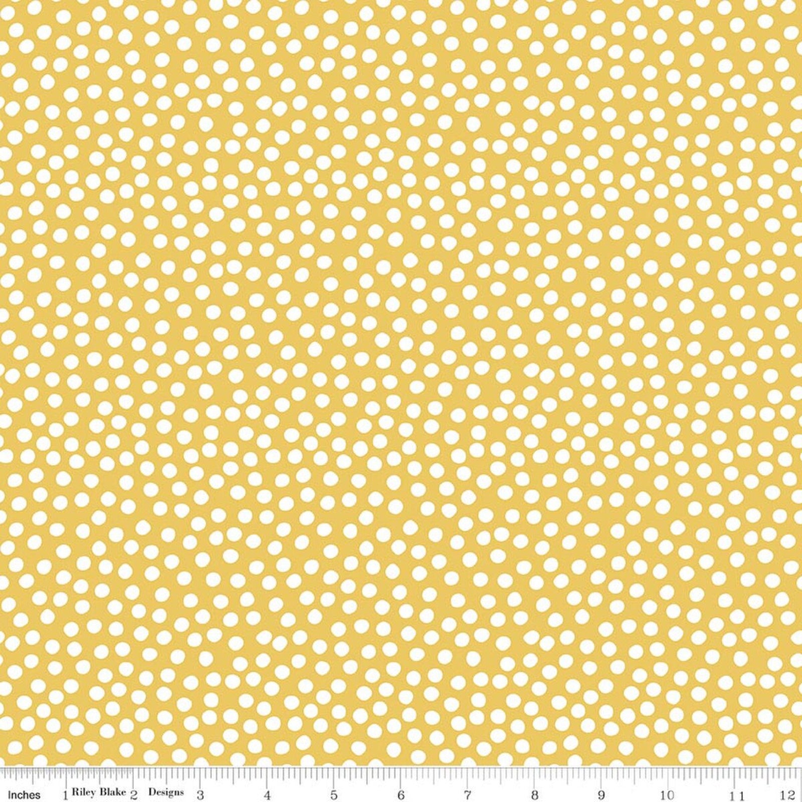A close-up of a fabric pattern featuring small white hand-drawn style polka dots on a warm mustard yellow background, with a measuring ruler visible along the bottom edge.