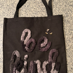 Black tote bag with tufted ‘be kind’ lettering and three small embroidered bees, demonstrating couching with large yarn.