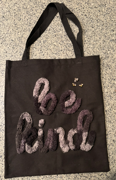 Black tote bag with tufted ‘be kind’ lettering and three small embroidered bees, demonstrating couching with large yarn.