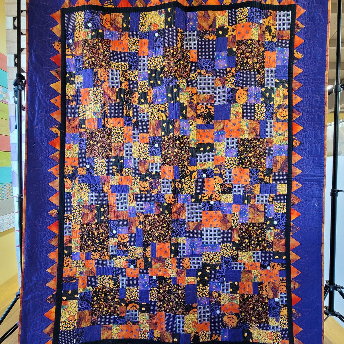 Scrappy crumb quilt featuring small patchwork pieces in Halloween‑themed fabrics with a purple and orange zigzag border