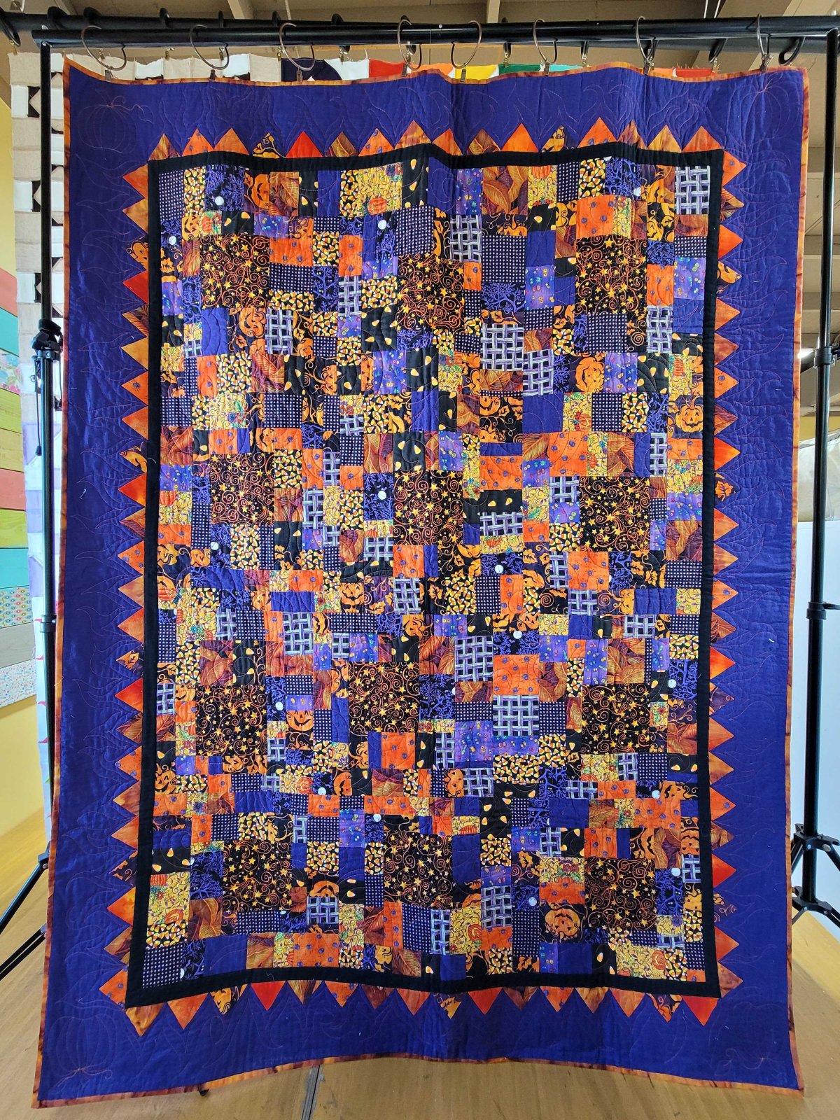Scrappy crumb quilt featuring small patchwork pieces in Halloween‑themed fabrics with a purple and orange zigzag border