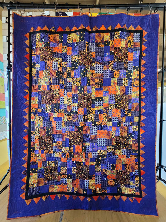 Scrappy crumb quilt featuring small patchwork pieces in Halloween‑themed fabrics with a purple and orange zigzag border