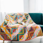 Curvy Log Cabin quilt draped over a teal sofa in bright modern colors.