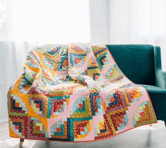 Curvy Log Cabin quilt draped over a teal sofa in bright modern colors.