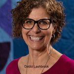 Headshot of Debbi Lashbrook wearing glasses and a magenta top in front of a blue and purple backdrop