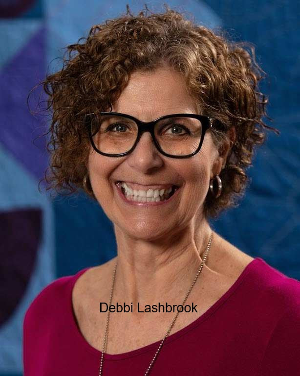 Headshot of Debbi Lashbrook wearing glasses and a magenta top in front of a blue and purple backdrop