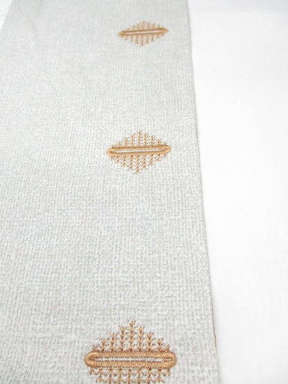 Light fabric with embroidered decorative buttonhole motifs stitched in golden thread.
