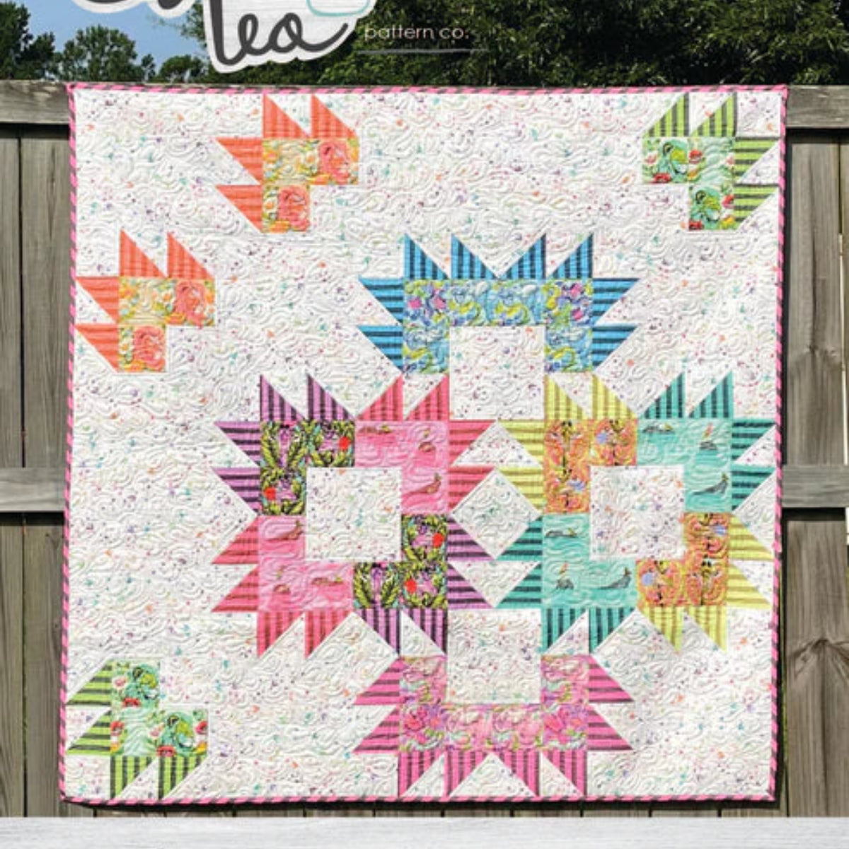 Colorful quilt with geometric patterns displayed outdoors, featuring the brand 'Sweet Tea Pattern Co'.