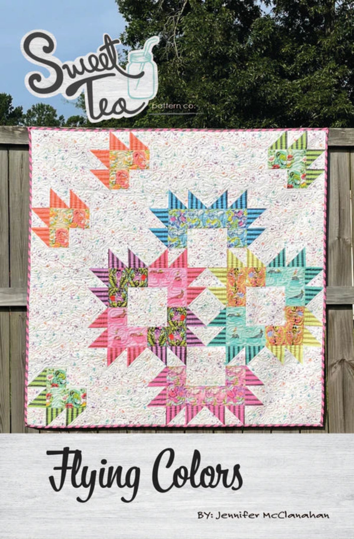 Colorful quilt with geometric patterns displayed outdoors, featuring the brand 'Sweet Tea Pattern Co'.