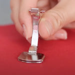 A close-up of a hand holding a silver sewing presser foot with #16 marking, positioned over red fabric.