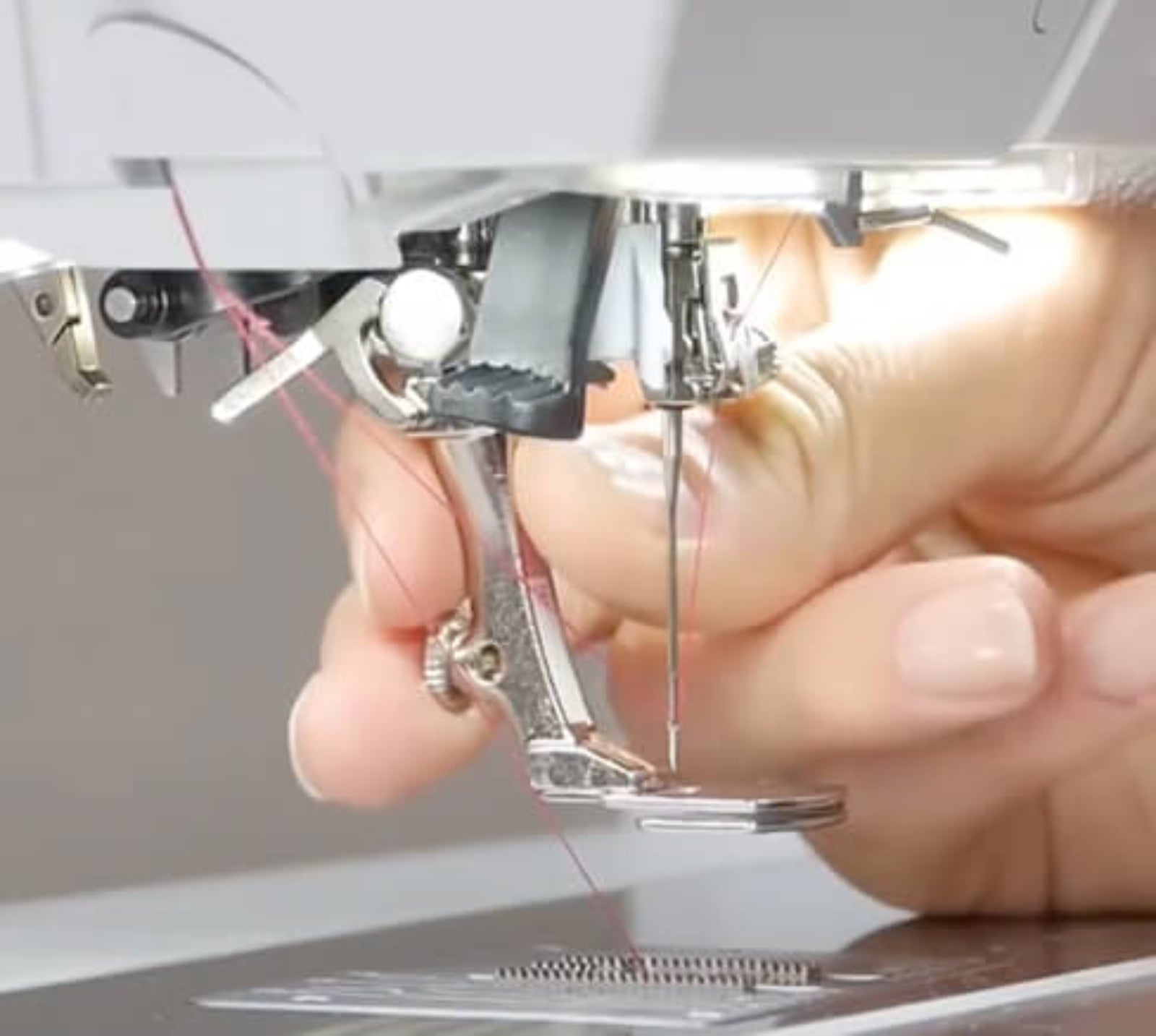 Close-up of a person's hand adjusting a silver metal sewing machine presser foot and thread under the needle area of a sewing machine.