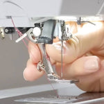 Close-up of a person's hand adjusting a silver metal sewing machine presser foot and thread under the needle area of a sewing machine.