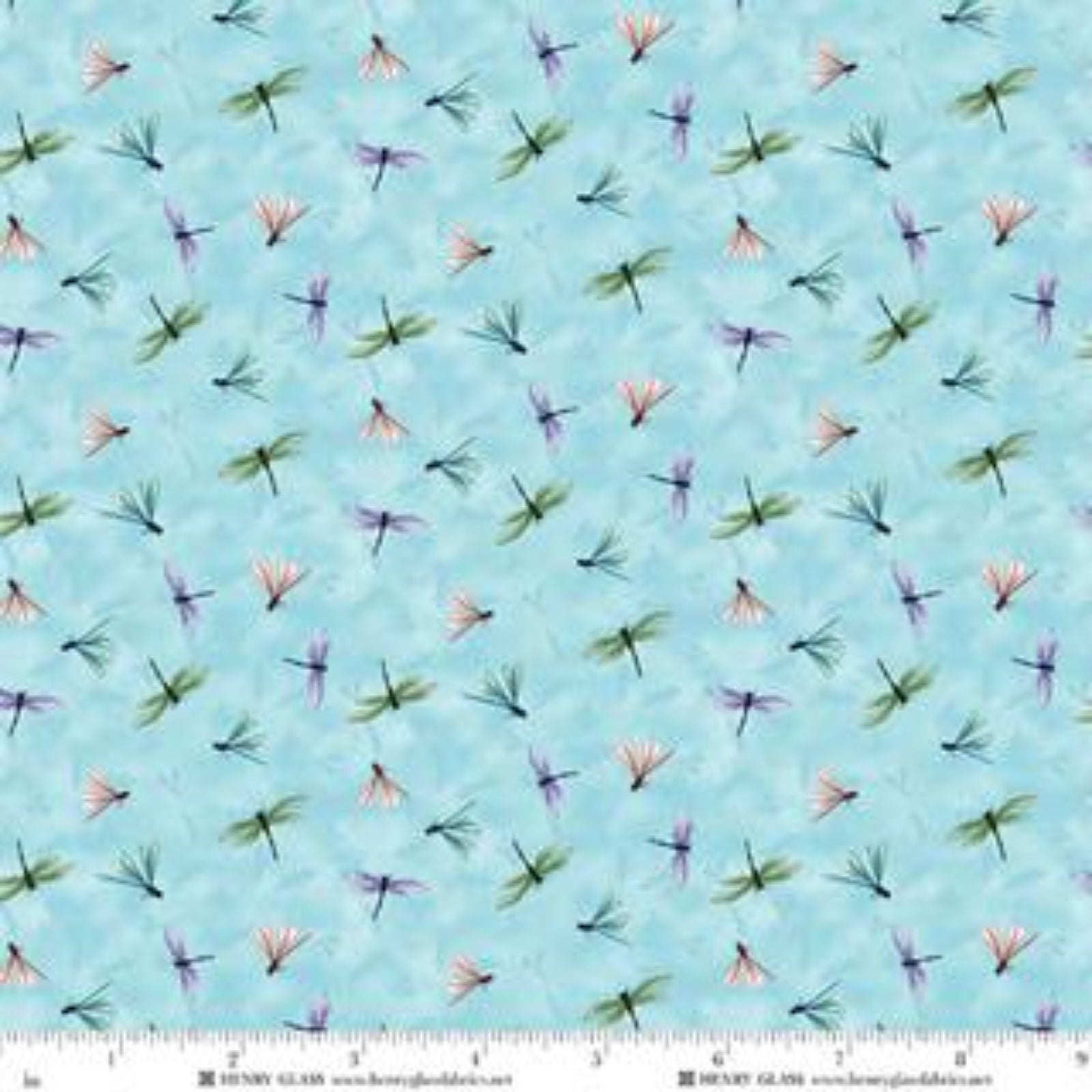 Light blue fabric with a repeating pattern of small dragonflies in green, purple, and pink, shown with a measuring ruler along the bottom edge.