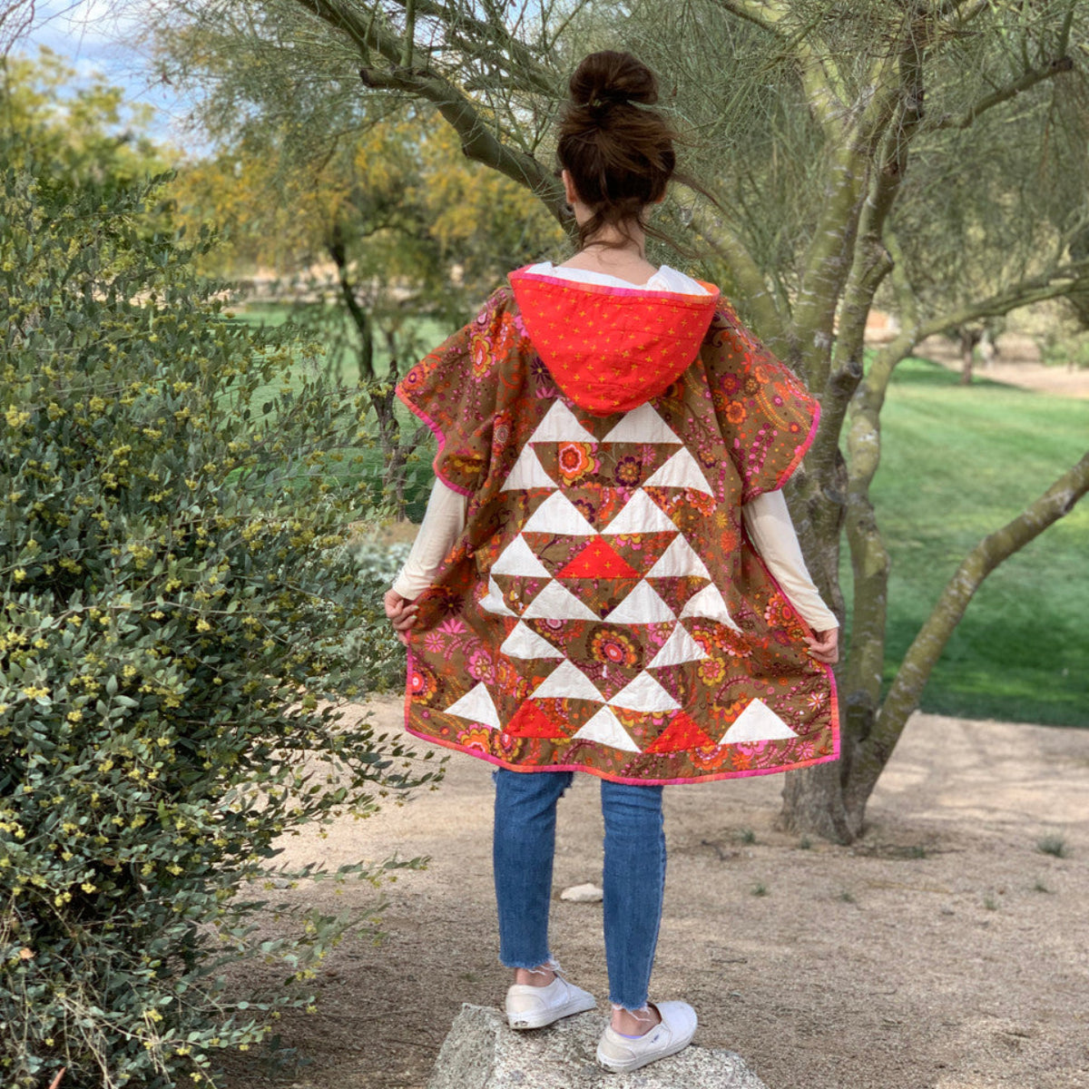 Person wearing a colorful quilted jacket in a natural setting with trees and greenery.