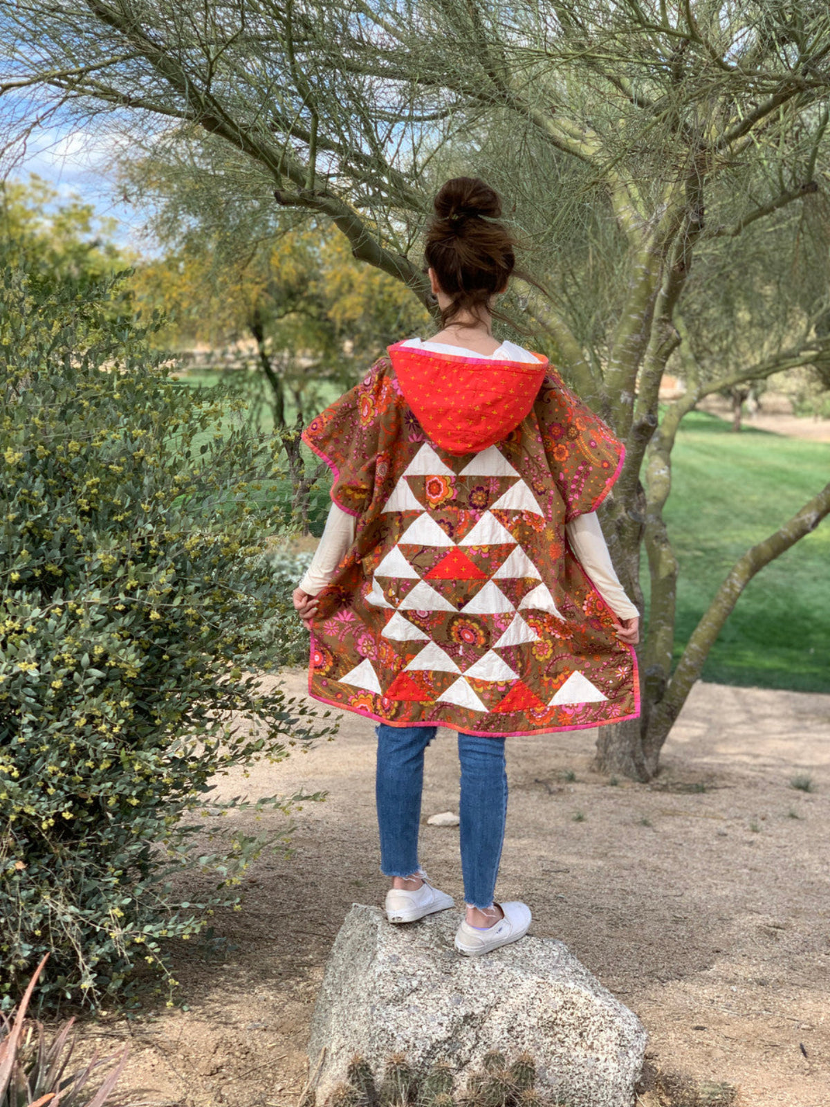 Person wearing a colorful quilted jacket in a natural setting with trees and greenery.