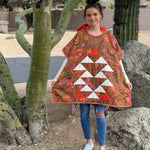 Person wearing a colorful quilted poncho standing outdoors with trees and rocks in the background