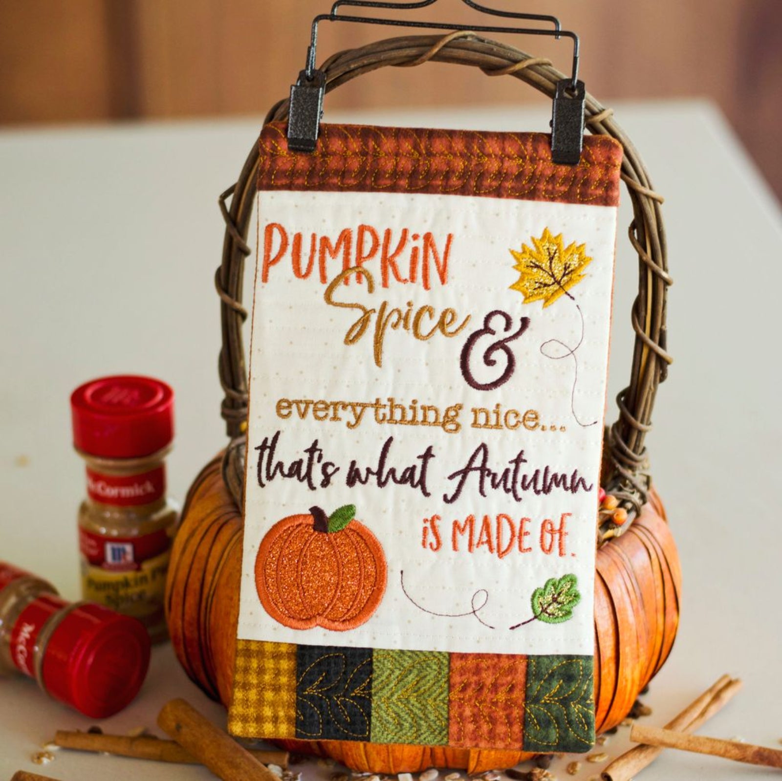 A decorative autumn-themed sign hanging from a basket handle, featuring the phrase 'Pumpkin Spice & everything nice.