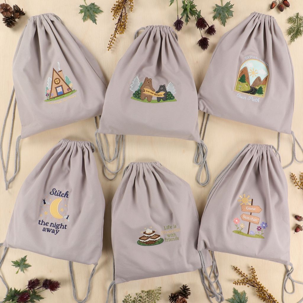 Set of six gray drawstring bags with embroidered designs on a beige background with decorative elements.