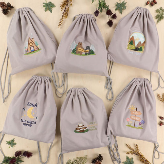 Set of six gray drawstring bags with embroidered designs on a beige background with decorative elements.
