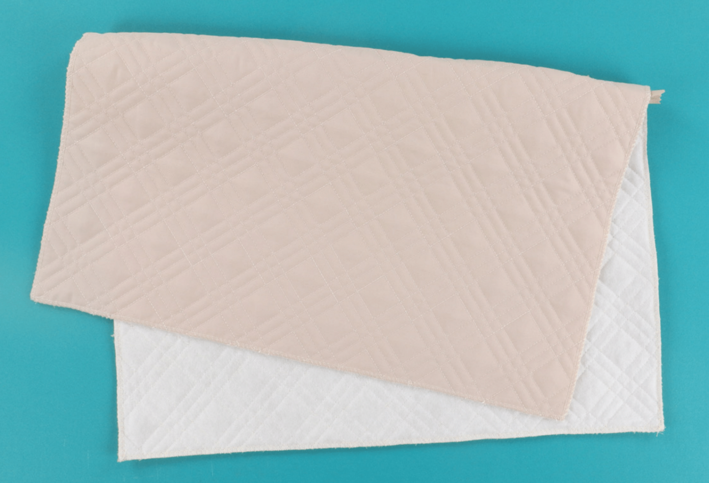 Two rectangular quilted fabric pads, one in light blush pink and one in white, stacked on a solid turquoise background.