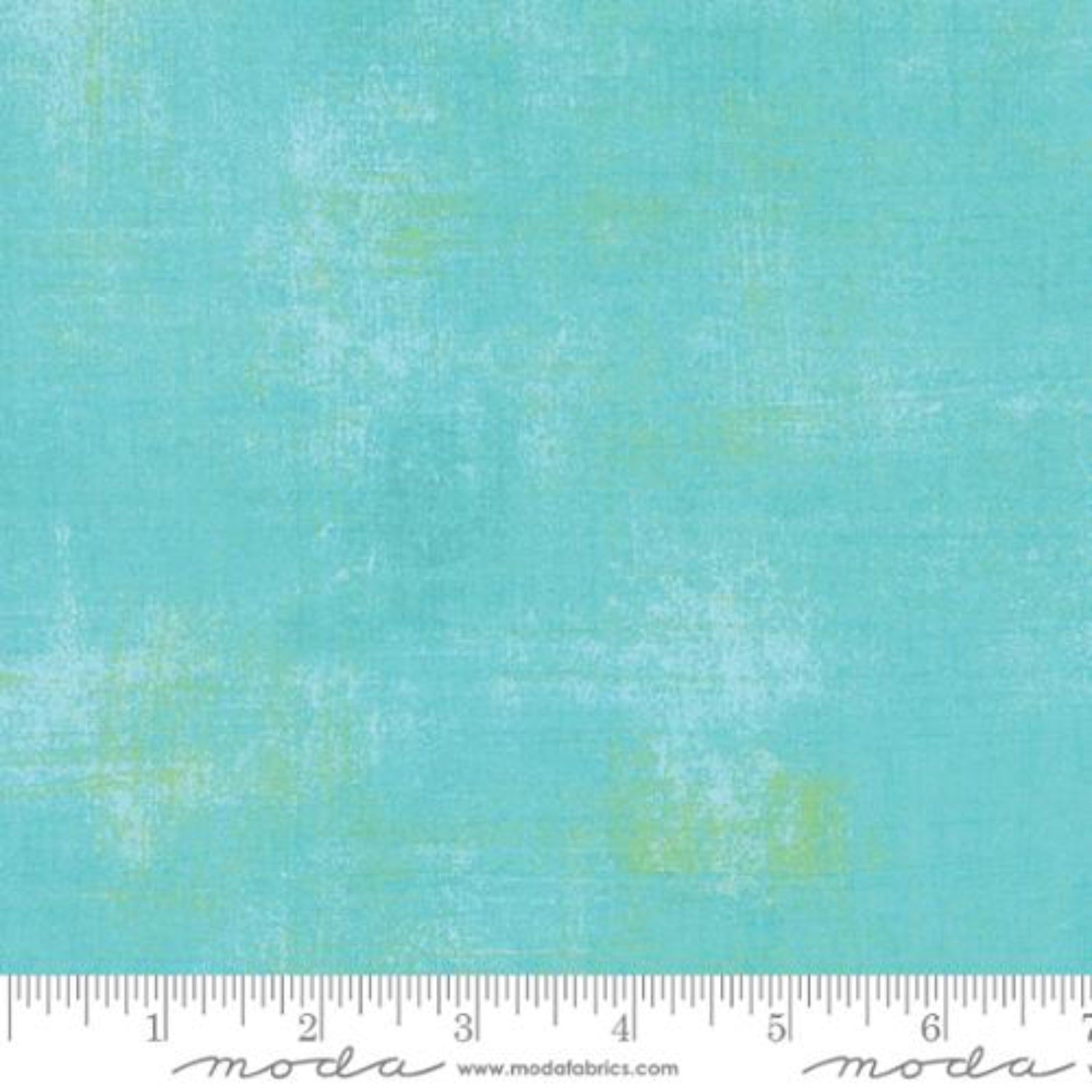 A close-up fabric swatch showing a textured turquoise blue surface with subtle pale yellow-green mottling. A white ruler along the bottom edge includes the Moda brand name and website.