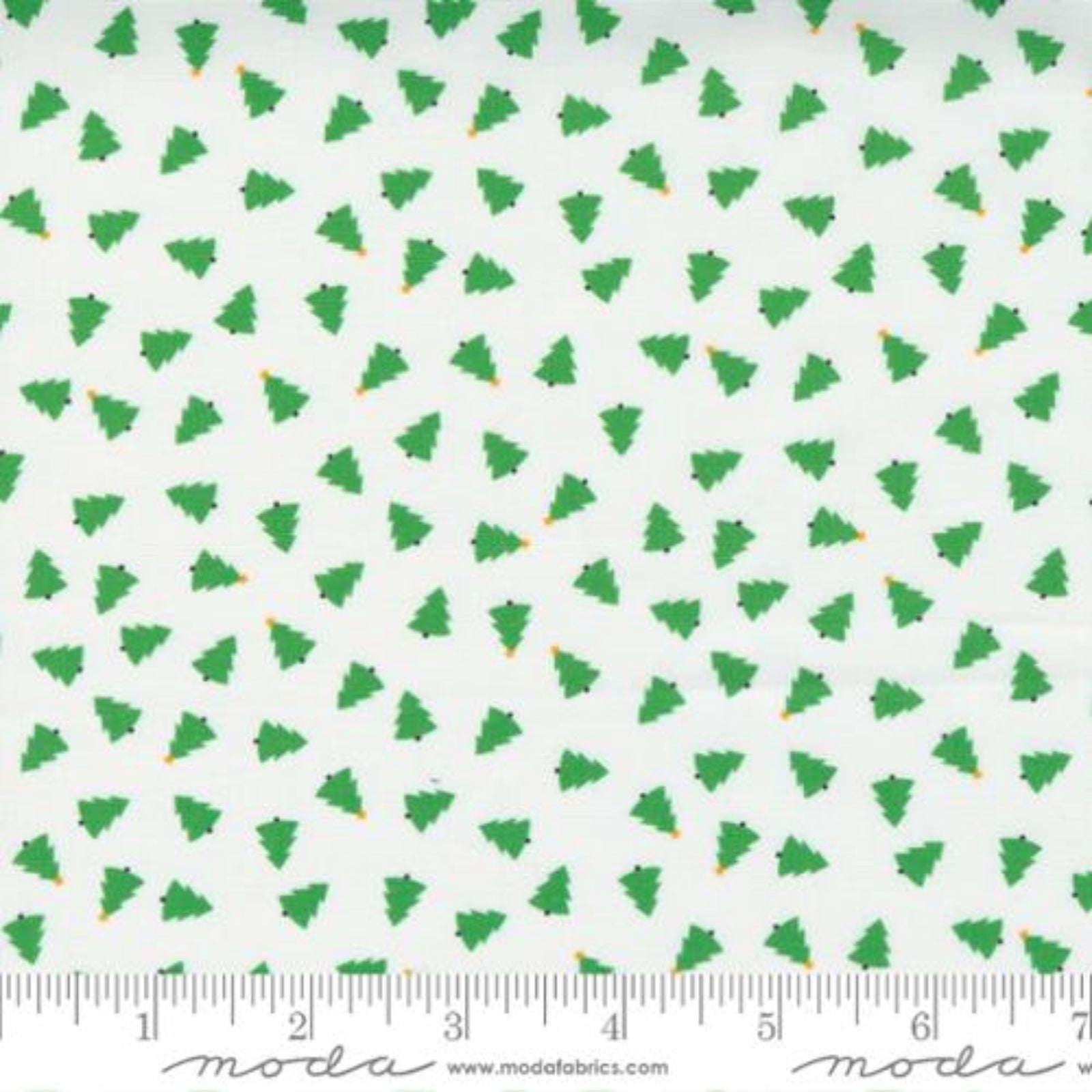 White fabric with a repeating pattern of small green Christmas trees, shown with a ruler at the bottom to indicate scale. The Modas Fabrics brand name and website are printed at the bottom.