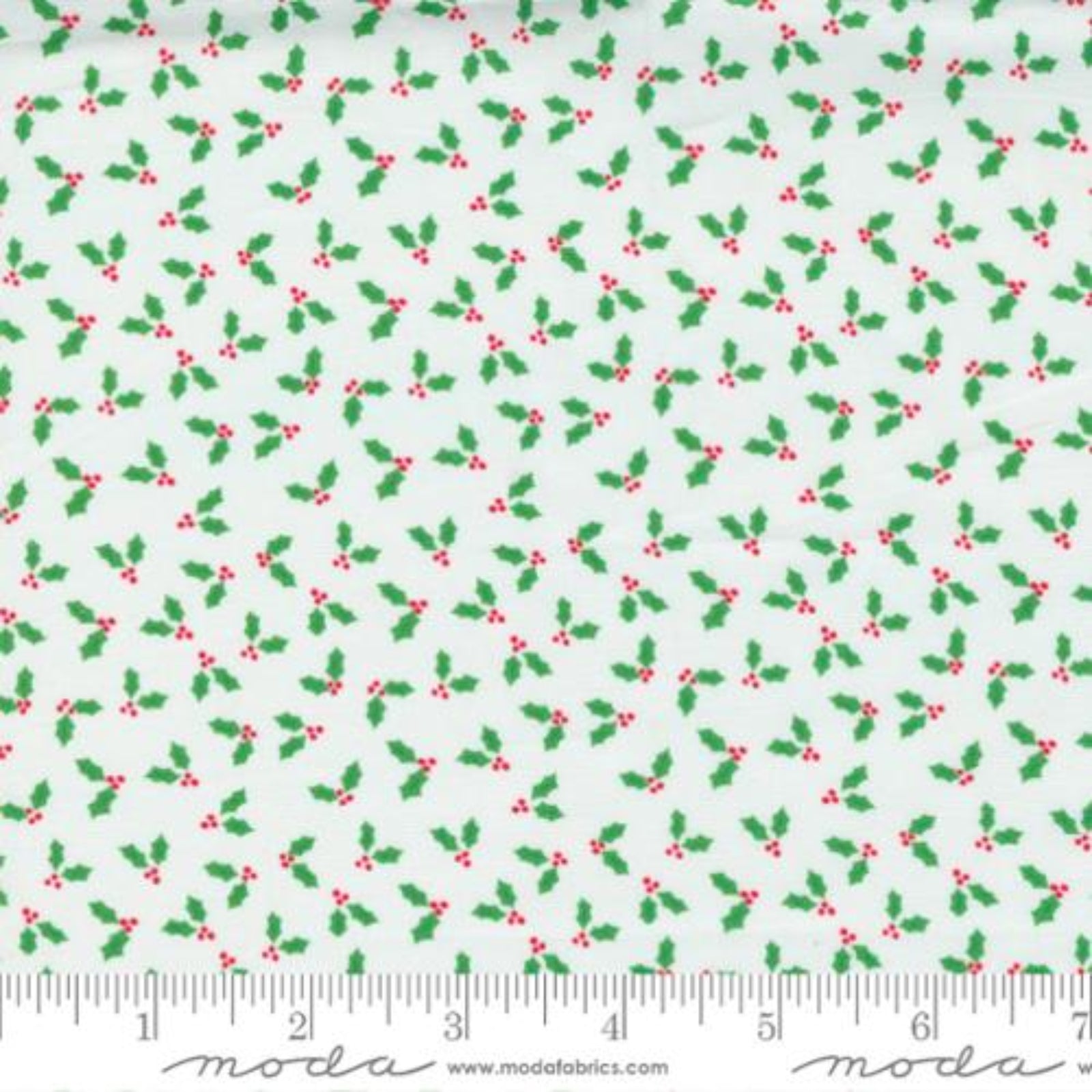 White fabric with a repeating green holly and red berry pattern, shown flat with a measuring ruler along the bottom edge.