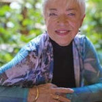 Outdoor portrait of instructor Nancy Chong seated in front of blurred green foliage.