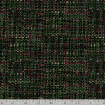 A close-up of a woven fabric texture with a dark green and black plaid pattern, accented with small pink and beige flecks. A ruler is visible along the bottom edge for scale.
