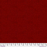 A close-up fabric pattern swatch showing a dense field of small dark red dots on a slightly darker red background, with a white ruler strip along the bottom edge for scale.