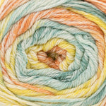 A close-up of variegated yarn wound into a spiral, showing soft pastel stripes of mint green, pale yellow, peach, and cream.