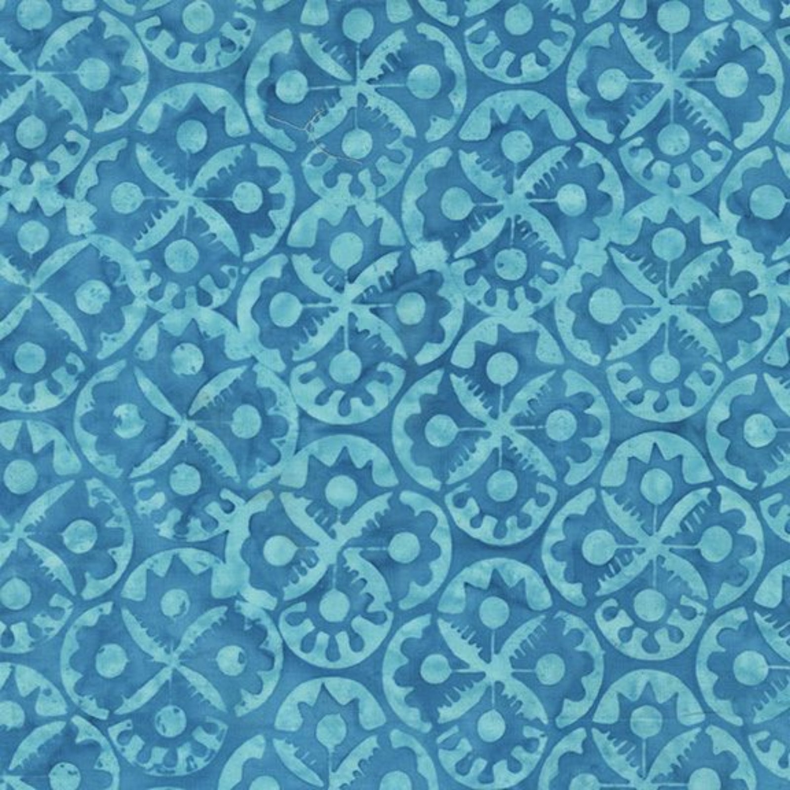 A close-up of a blue batik fabric with a repeating geometric and floral block-print pattern in light turquoise blue.