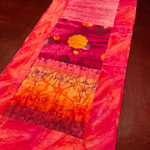 Quilted table runner in red, pink, and orange tones featuring floral motifs and decorative stitching.