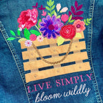 Close-up of a blue denim garment featuring a colorful embroidered basket of flowers and the text 'LIVE SIMPLY bloom wildly' on the back.