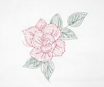 Pink and green embroidered flower design on white fabric, used to demonstrate reduced‑density stitching.