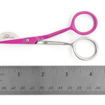 Pink and silver scissors with a circular ring handle, shown above a metal ruler on a white background. The brand name 'Tula PINK' is engraved on the blade.