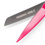 A close-up of a pink-handled fabric sharpener with a silver metal blade engraved with the words 'FABRIC ONLY', set against a plain white background.