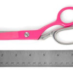 Bright pink scissors with silver metal blades and handles, shown next to a metal ruler on a white background.