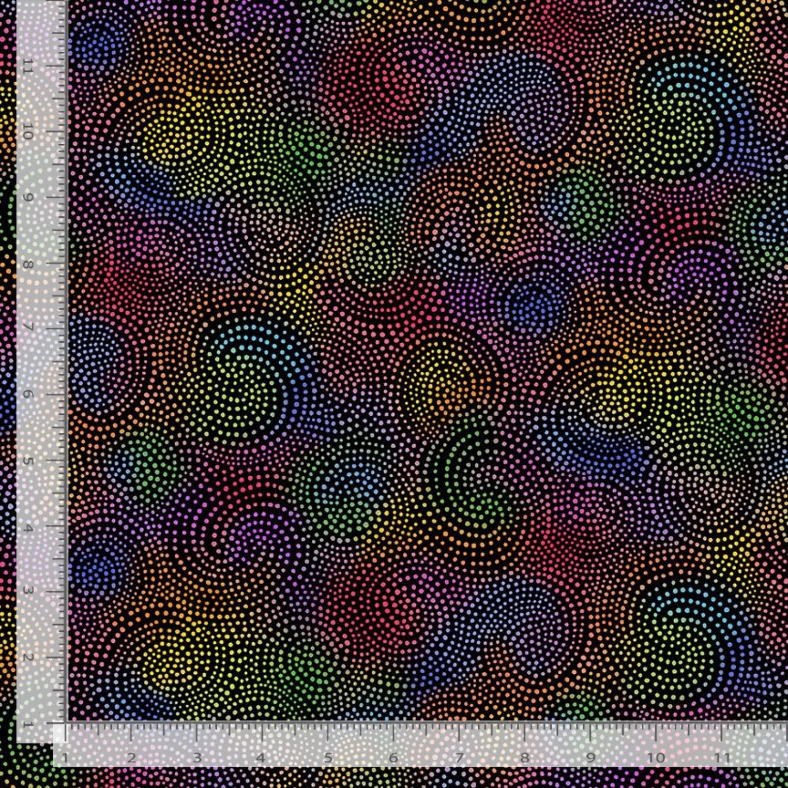 A close-up of patterned fabric with a dense dot design in many colors, including yellow, green, blue, purple, red, and orange, arranged in swirling circular motifs on a dark background. A white ruler is visible along the left and bottom edges for scale.
