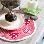 Cupcake on a decorative plate with heart patterns on a wooden table.