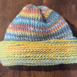 Tunisian crochet hat with a folded brim, worked in speckled yellow yarn and topped with pastel striped Tunisian stitches.