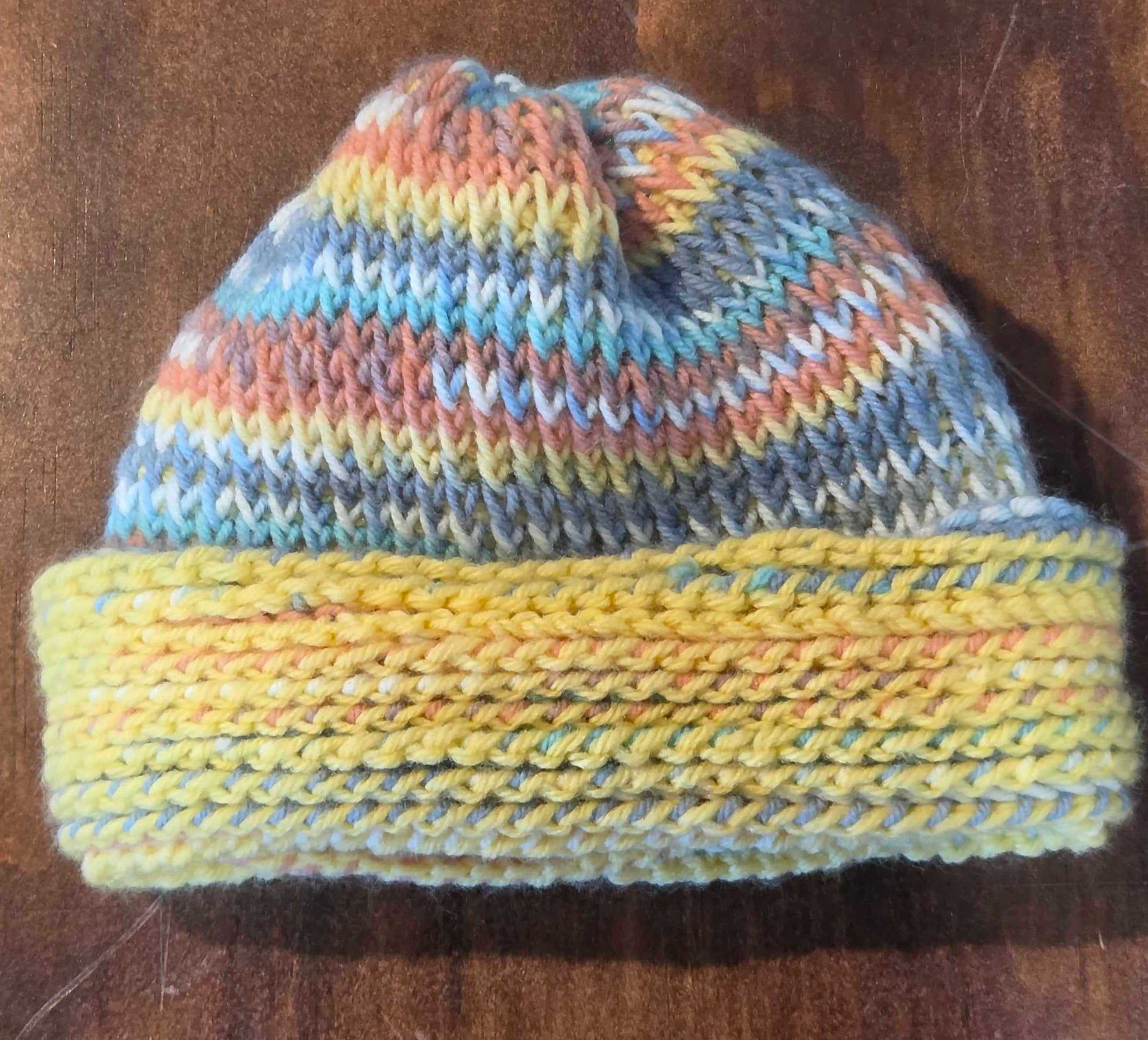 Tunisian crochet hat with a folded brim, worked in speckled yellow yarn and topped with pastel striped Tunisian stitches.